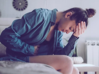 Kobieta siedząca na łóżku trzymająca się za brzuch